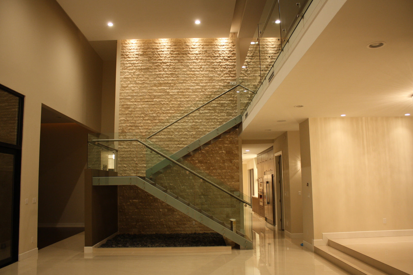 Sculptural staircase with glass railing and a stone feature wall in a Lemar home
